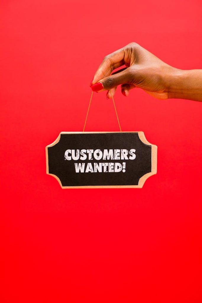 Close-up of a hand holding a Customers Wanted sign against a bright red background.